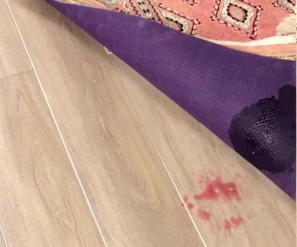 Rug corner lifted on an ordinary purple rug pad: the wine soaked through the pad and is on the wood floor